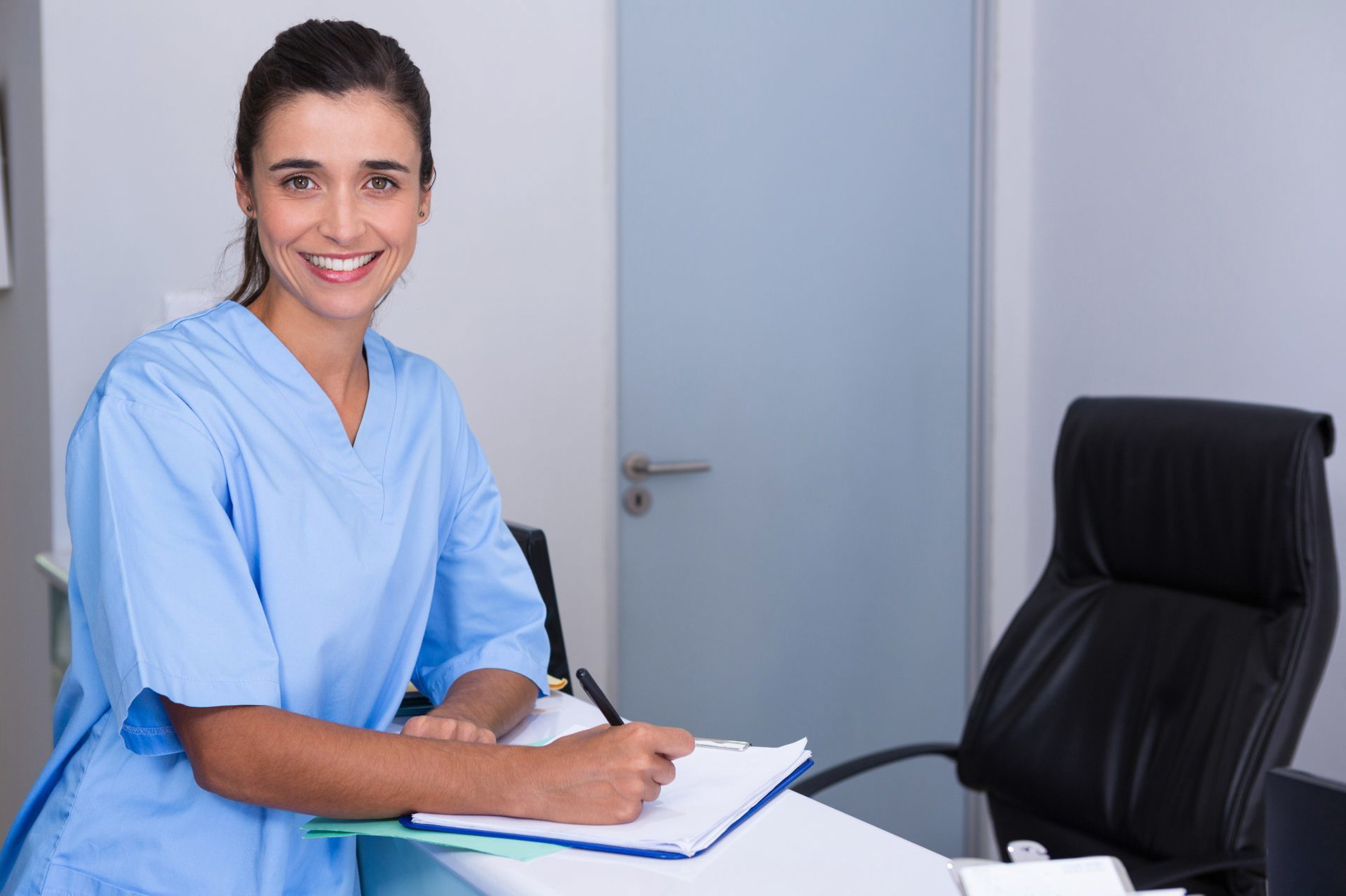 Women in scrubs sitting at a desk taking notes. 