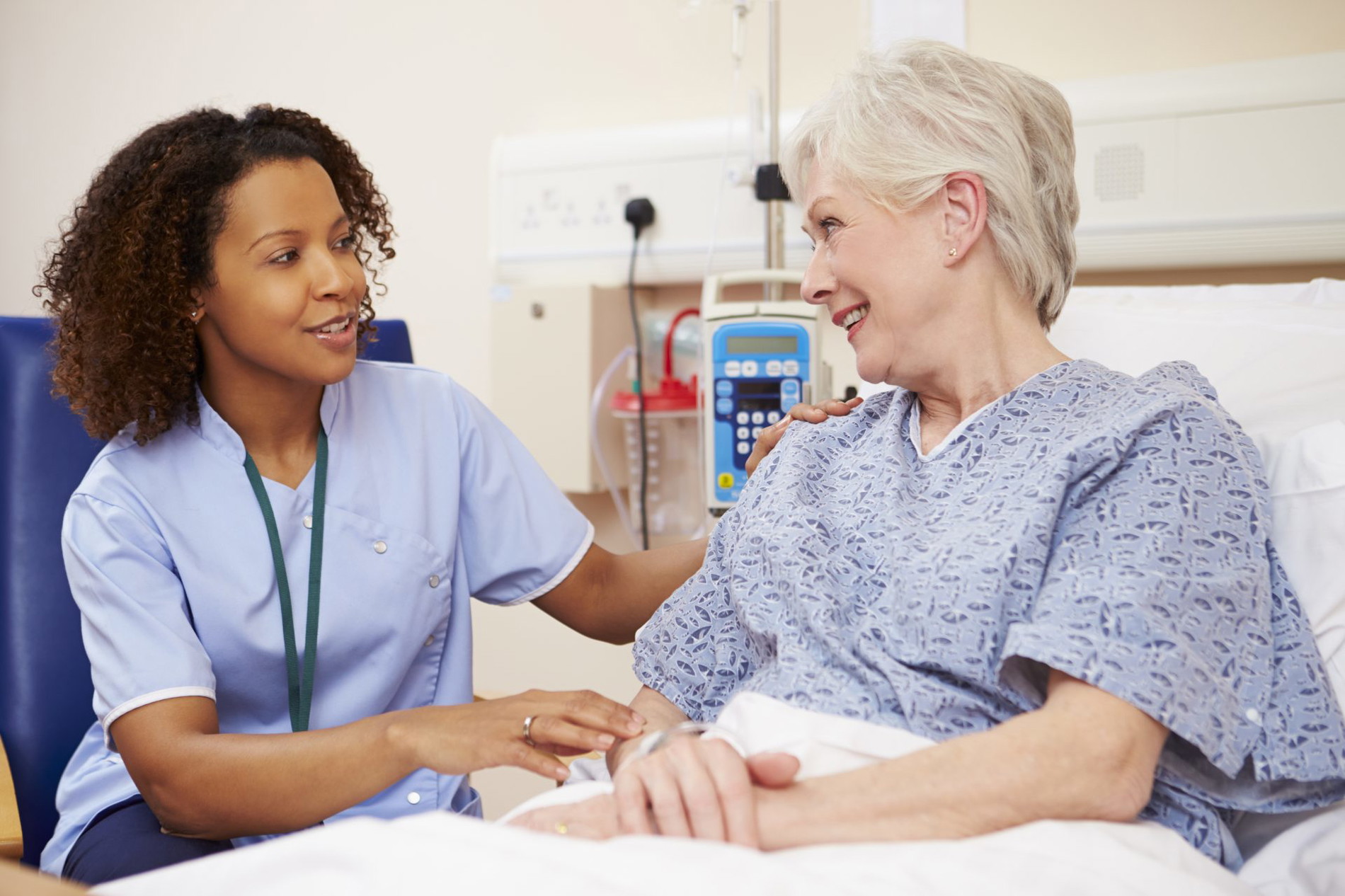 Patient in a hospital bed with a caregiver sitting next to her.